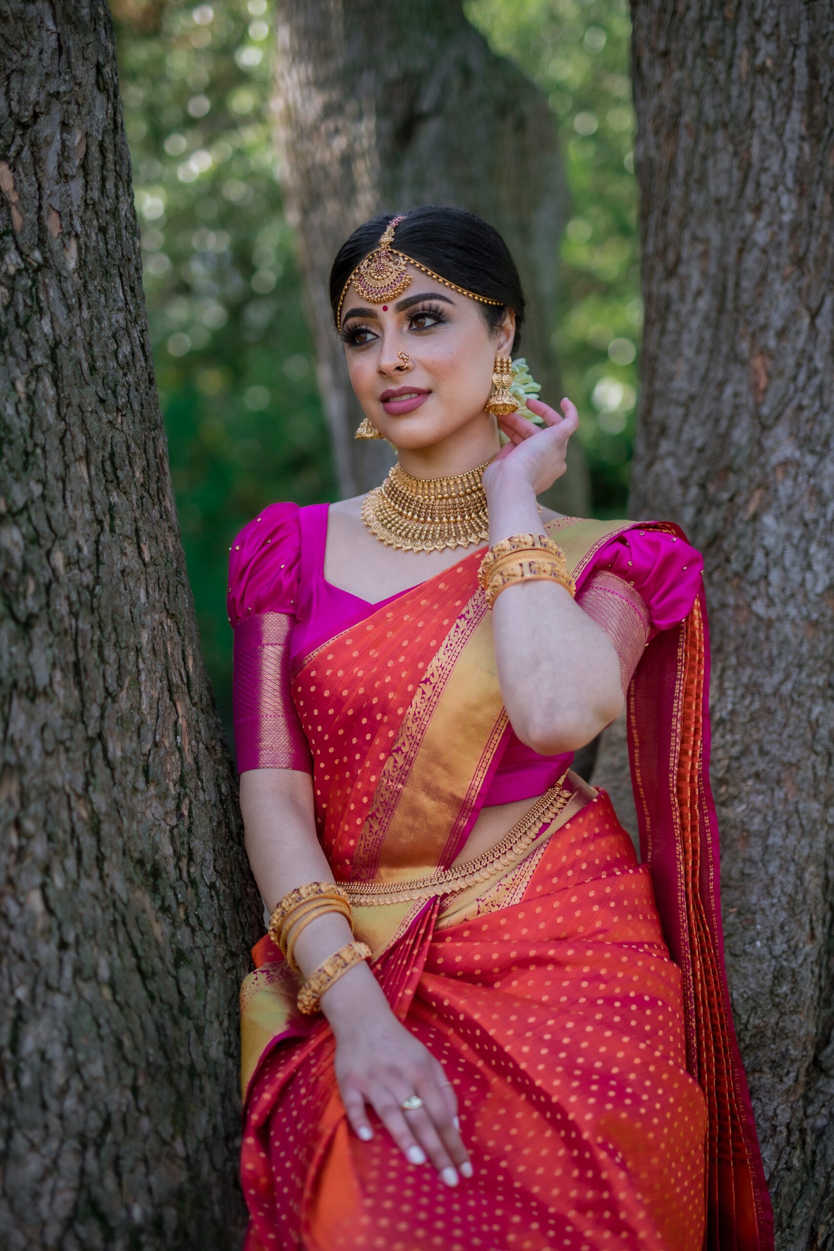 Bride posing wearing orange Saree by the tree